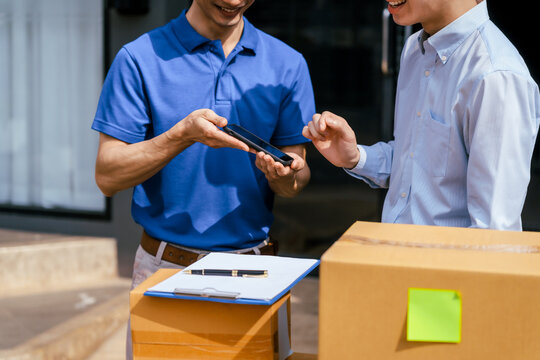 Two men in business casual clothes check a smart phone beside cardboard boxes and a clipboard during a package delivery hand off.