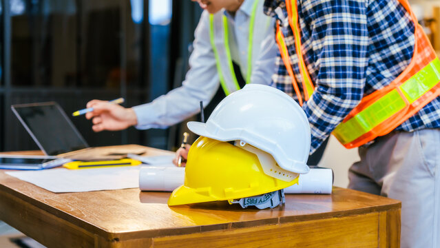 Construction team meeting with hard hats, laptop and blueprints on a desk, showing planning, safety and teamwork at a worksite
