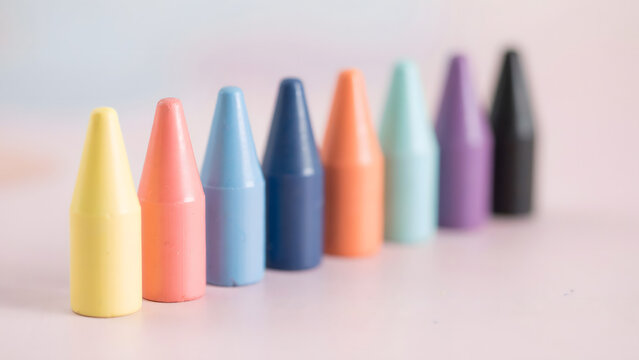 A row of colorful wax crayons standing upright on a soft pink surface