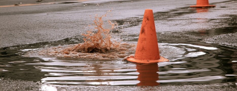 Traffic cone in flooded water on paved street with splashing debris  