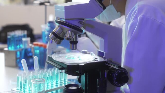 Scientist using a microscope in a modern laboratory with test tubes and glassware under blue light