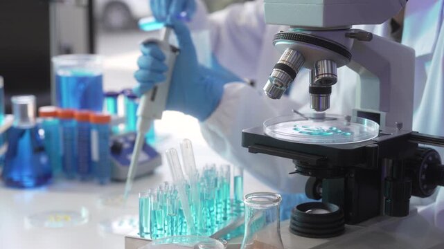 Scientist using a pipette near a microscope with test tubes and blue liquid in a modern laboratory