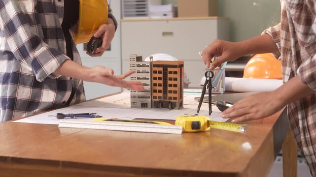 Two construction workers measuring an architectural model with tools on a table in an office or studio