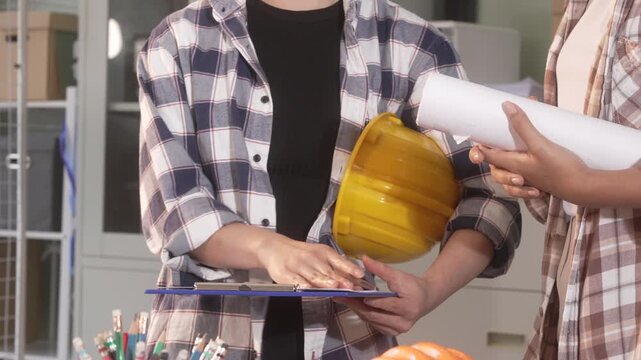 People discussing construction plans indoors with hard hat, clipboard and rolled drawings