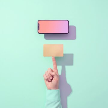 Hand balancing blank golden credit card under smartphone on pastel mint background, online mobile payment and digital finance concept