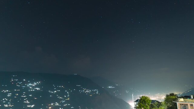 4K Night Lapse shot of stars moving above the Kullu valley with villages on it as seen from Peej Village near Kullu, Himachal Pradesh, India. Scenic view of stars above the Himalayan mountains.