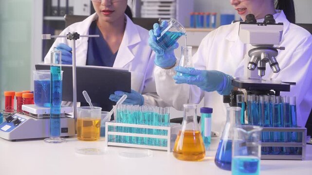 Two scientists working together in a laboratory with a microscope, laptop, test tubes, and glass flasks during medical research