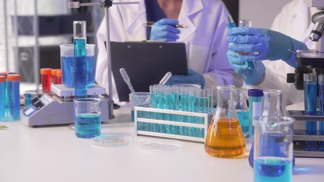 Scientist working in a laboratory with test tubes, flasks, microscope and tablet during medical research.