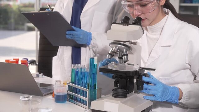 Scientists in a laboratory examining samples with a microscope, test tubes, clipboard, and safety goggles