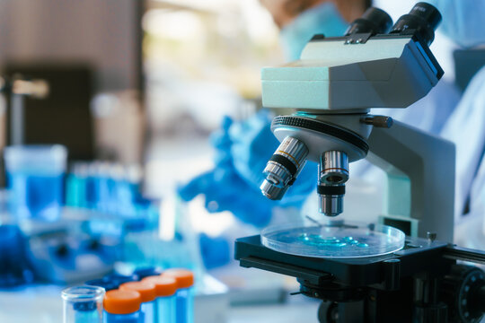 Modern microscope in a laboratory with test tubes and blurred scientist in the background, showing medical research and analysis