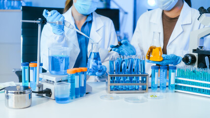 Fototapeta premium Scientists working in a medical laboratory with test tubes, pipette, beakers, and microscope, handling blue liquid for research and testing