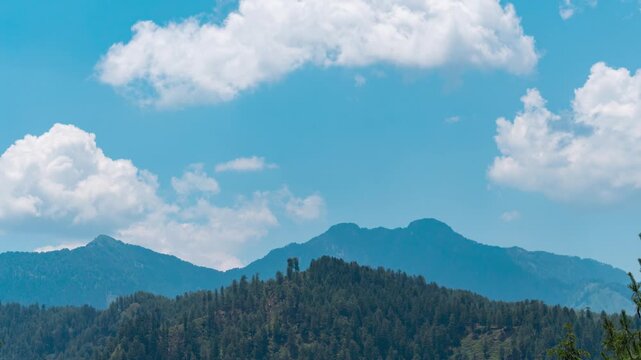 4K Time Lapse shot of clouds above the Himalayan mountain range with pine trees on top of them as seen from Kais Dhar near Lot Village in Himachal Pradesh, India. Scenic view of mountains in summer.