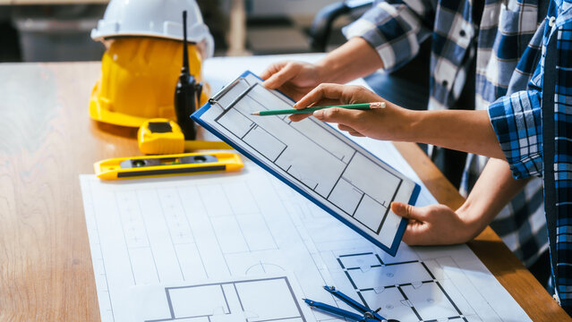Architects or builders reviewing house plans at a desk with safety helmet, level tool and pencils, showing teamwork, planning and construction work in a modern office.