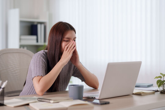 Stressed young Asian businesswoman covering face in frustration while working on laptop at home office desk with copy space