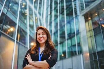 Fototapeta premium Confident businesswoman smiling with arms crossed standing in modern financial district