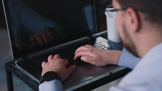Man typing on laptop takes sip of coffee and continues work on computer completing online tasks and remote work in calm home environment