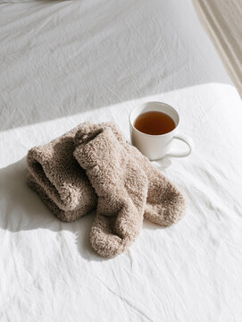 Plush beige sock and chamomile tea on white linen, minimalist still life for calm sleep routine with soft sunlight and empty space