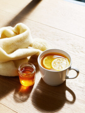 White tea lemon tea honey jar cream scarf wooden table warm light morning sun still life winter care cozy mood ceramic cup lemon slice glass jar hot drink soft shadow bright room natural light