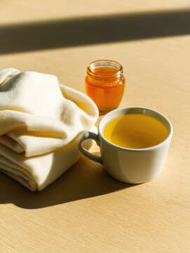 Cream scarf white mug honey jar lemon tea wooden table still life warm light soft shadow winter care minimalist style