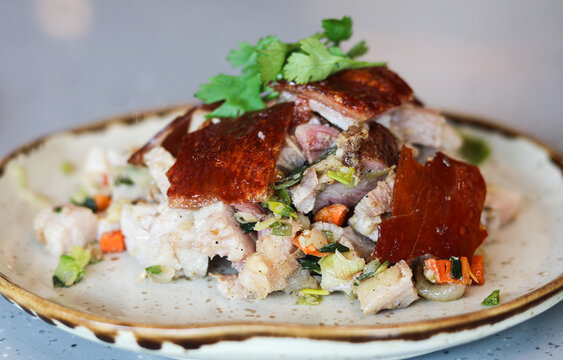 A closeup portion of sliced roasted suckling pig served on a ceramic plate.