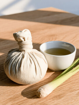 Herbal compress cotton pouch tea cup lemongrass wooden table natural light still life wellness therapy minimal