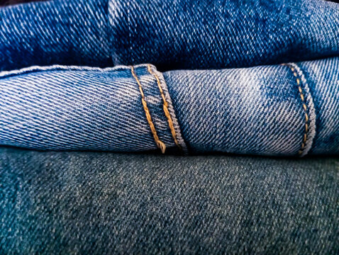 close-up of folded denim blue jeans showing detailed fabric texture, twill weave pattern, and yellow stitched seam seams.