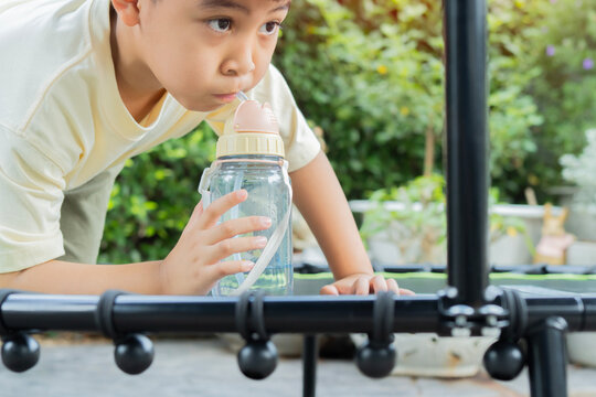 A thirsty boy taking a water break after playing mini trampoline at outdoor.
