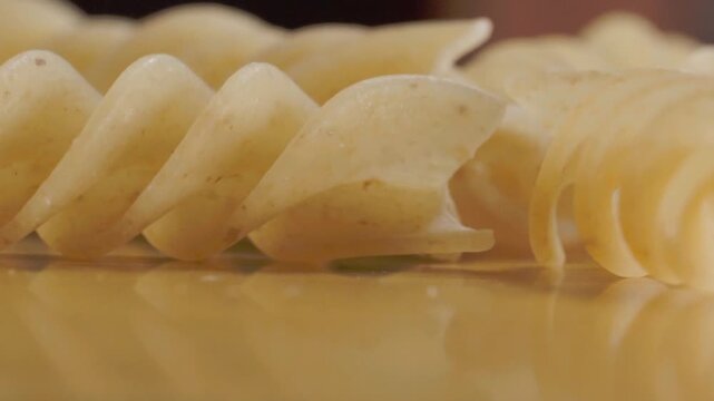Macro close up of uncooked fusilli pasta arranged on wooden table with shallow depth of field. Dry pasta featuring spiral shape, smooth texture and natural color for food preparation.