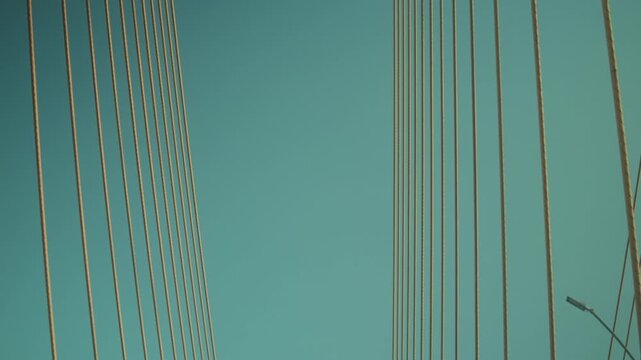 Upward view of a modern cable-stayed bridge filmed from a moving vehicle. Dynamic transportation infrastructure scene featuring geometric lines, engineering, and urban travel.