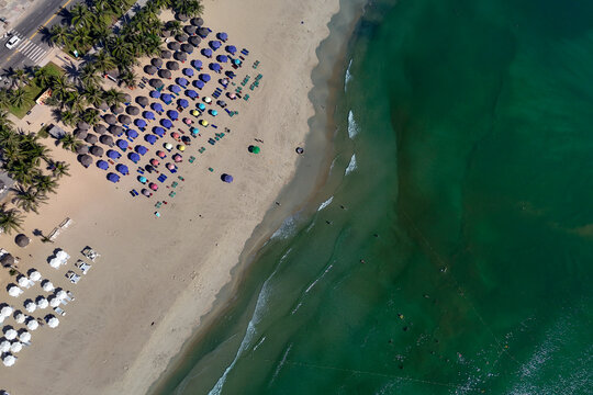 Umbrellas on a city sandy beach rest on the shore and near the gentle waves of the clear ocean