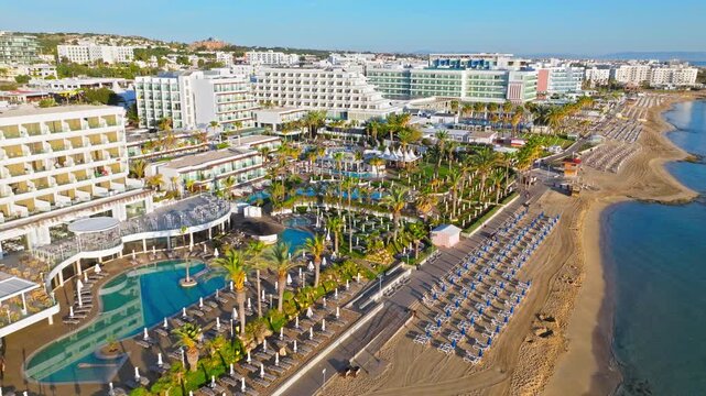 Drone view of Protaras beachfront in Cyprus. Sandy beach, resort hotels, coastal road and blue Mediterranean water fill the sunny panorama.