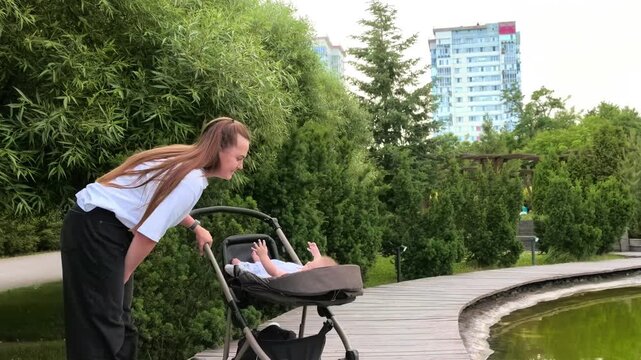 Mother leans over her baby in a stroller during a park walk, attentive parenting, maternal care, family bonding, peaceful outdoor lifestyle.