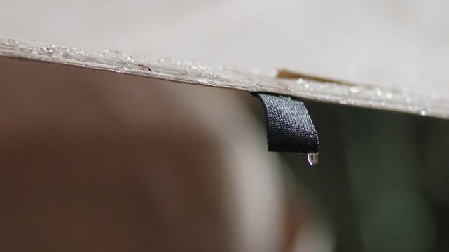 Extreme close up of raindrops covering a camping tarp surface. Wet black loop gear with blurry soft green and brown background during rain.