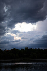 A break in deep storm clouds reveals a glowing window of light above a calm river with soft reflections hinting at clearing weather beyond the dark textured ceiling © Chornogirskyi