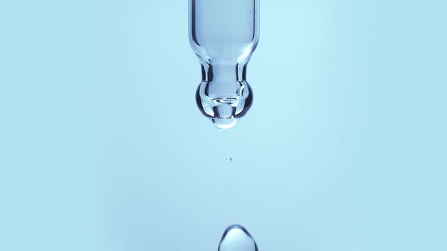 Macro shot of a blue copper peptide or hyaluronic acid serum droplet falling from a glass pipette dropper in slow motion isolated on a solid light blue background