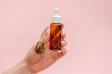 Woman's hand holding glass cosmetic bottle with snail. Mockup for your brand. Skin care product, spa, luxury, natural beauty © Antonio