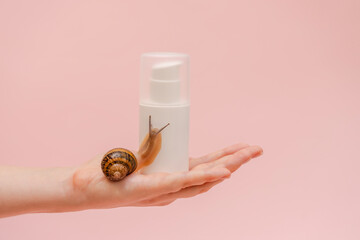 Elegant hand with cosmetic white bottle with snail. Mockup for your brand. Skin care product, spa, luxury, natural beauty © Antonio