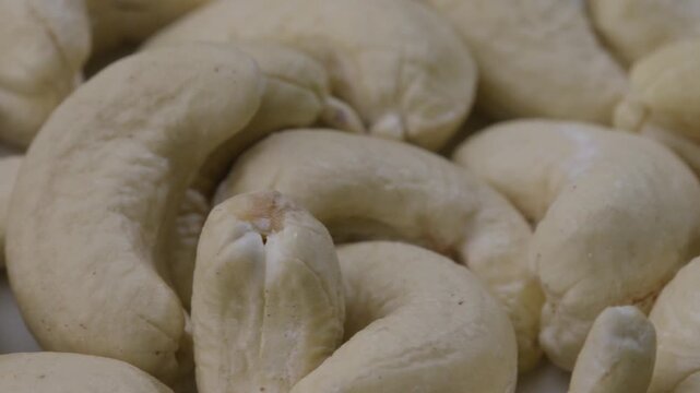 Extreme macro panning camera shot moving smoothly across a pile of fresh whole raw cashew nuts, showcasing premium dry fruit texture, healthy nutrition, and organic food quality.