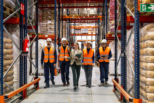 Diverse team of warehouse workers and a female manager walking through aisles of a busy logistics and distribution center