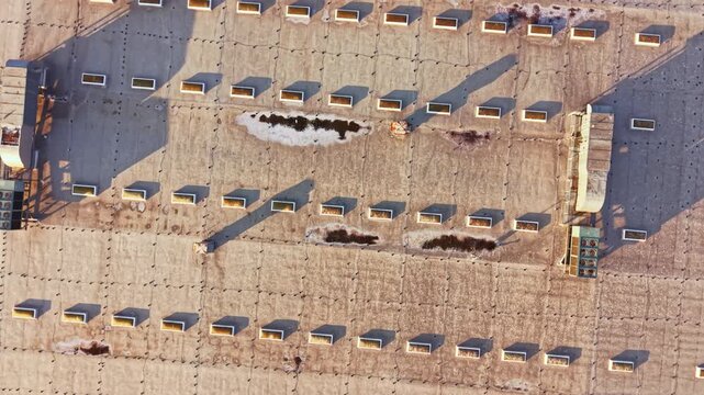 Workers are seen on a construction site in a city at early morning. Various materials are organized in rows. Shadows cast from equipment show the time of day.