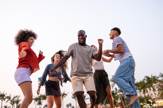 Energetic young people dancing with joy on the sandy beach at sunset, celebrating summer and freedom