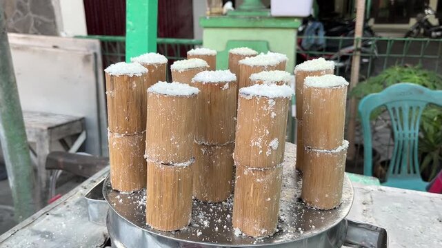 Traditional Indonesian kue putu rice cakes being steamed inside bamboo tubes on a metal steamer, popular local Asian street food vendor process.