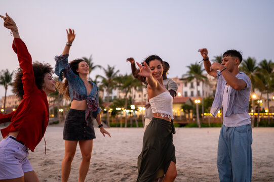 Happy young people embracing the beach lifestyle, dancing barefoot in the sand, celebrating freedom