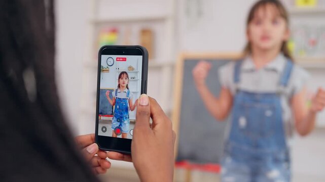 African teacher use phone record young child dancing in learning space.