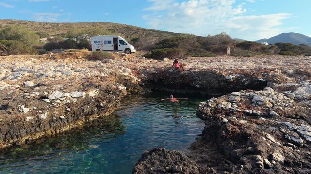 A couple relaxes by the ocean natural pool, a man and a woman from above drone view, Paros, Greece, where turquoise waters meet rocky shores. Perfect for relaxation and swimming