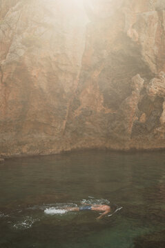 Swimmer gliding below sunlit cliffs at Kalypso Beach in Mediterranean