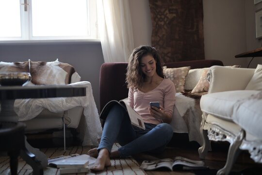 Smiling woman sits on floor with phone and magazines