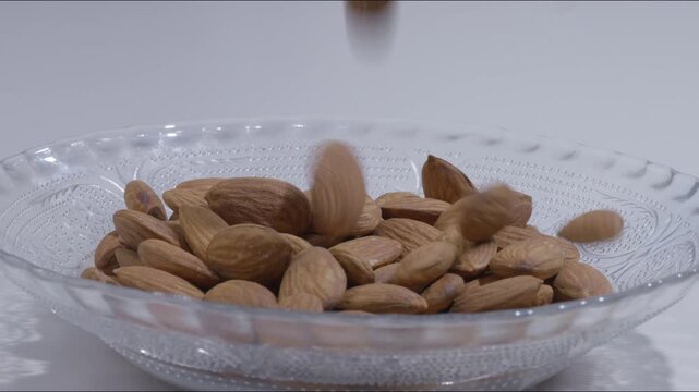 Slow motion video of fresh crunchy almonds falling and filling a decorative glass bowl, highlighting dynamic food motion, healthy dry fruit snacks, and organic nutrition.