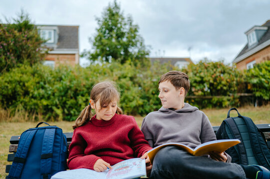 Boy and girl sitting together on a park bench with an open notebook