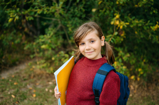 Smiling girl holding school notebook and wearing a backpack outdoors